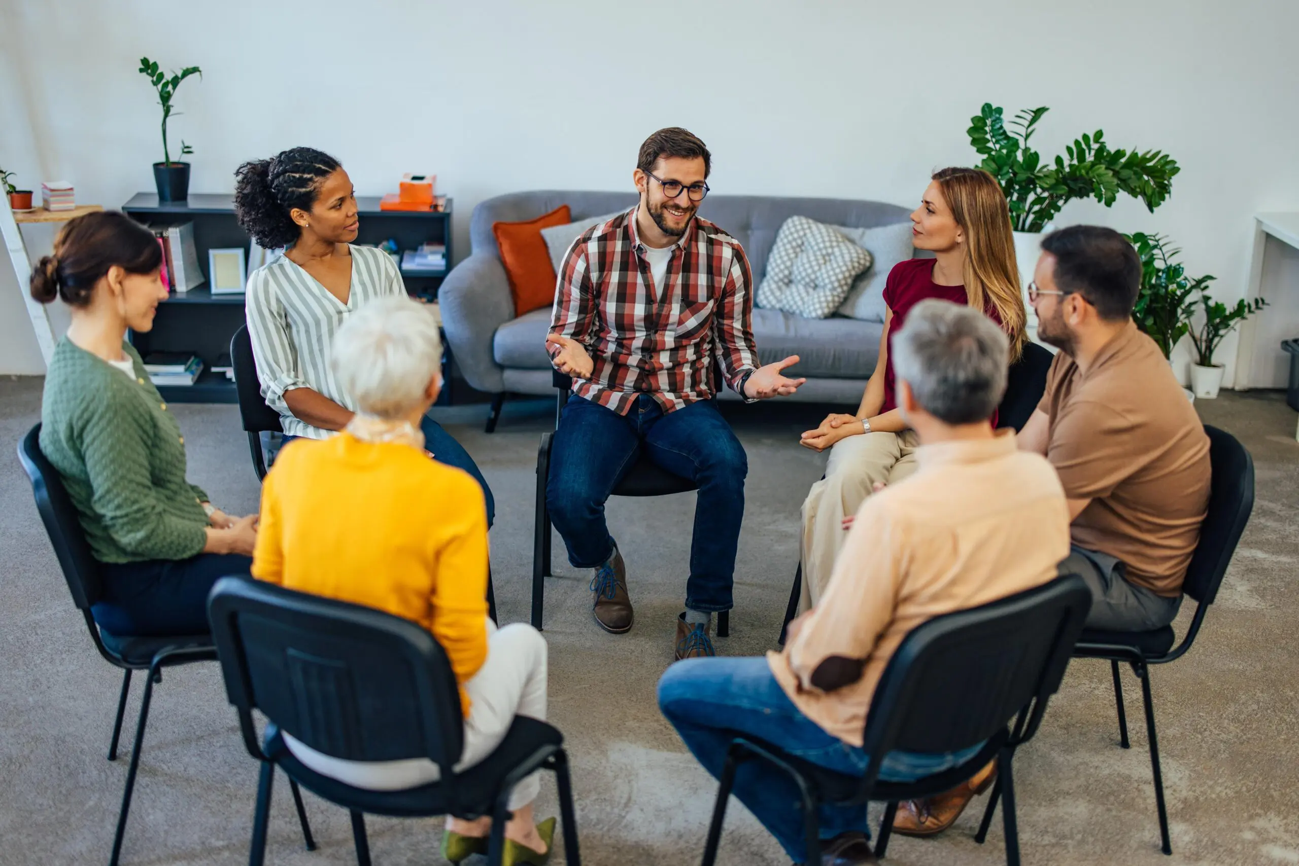 A group therapy session with six people seated in a circle, engaging in discussion.
