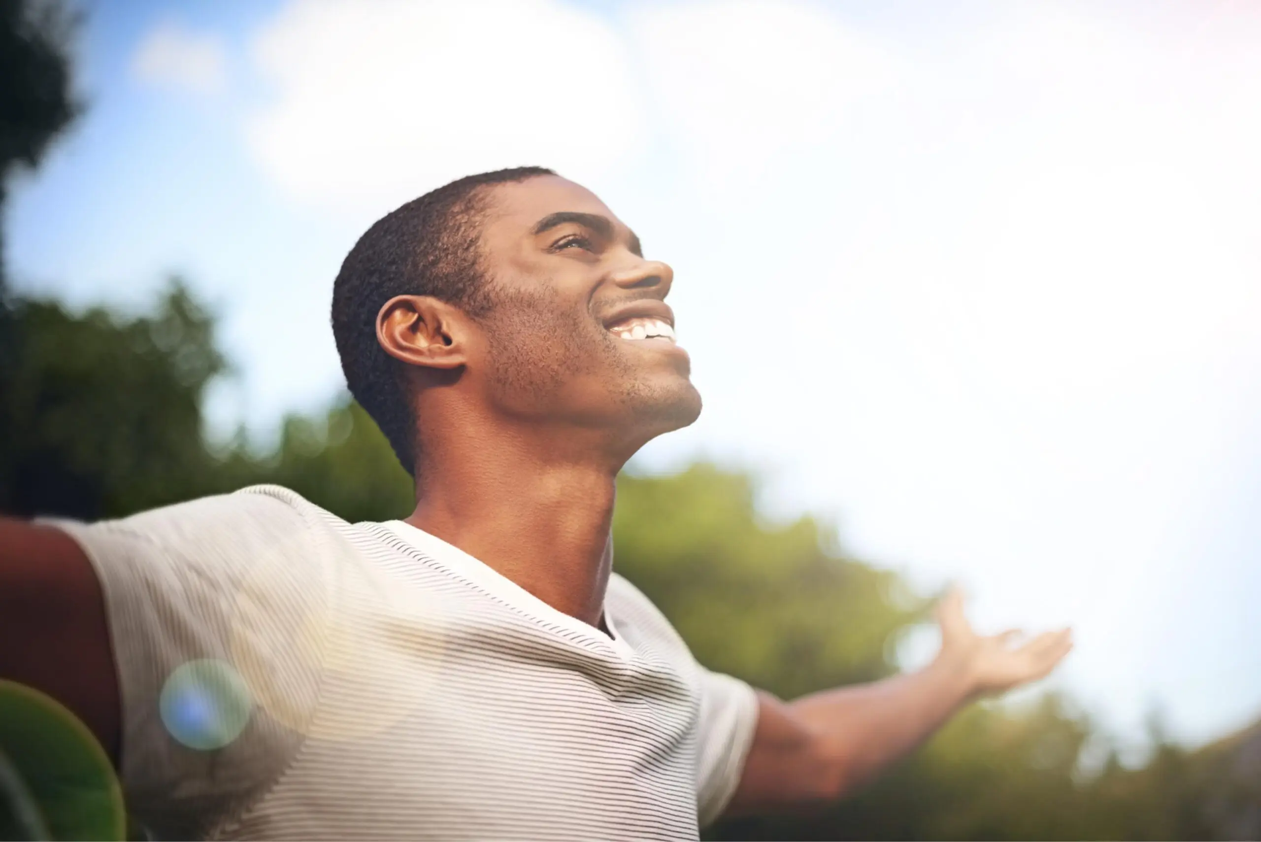 A joyful man with arms outstretched, smiling in the sunlight.