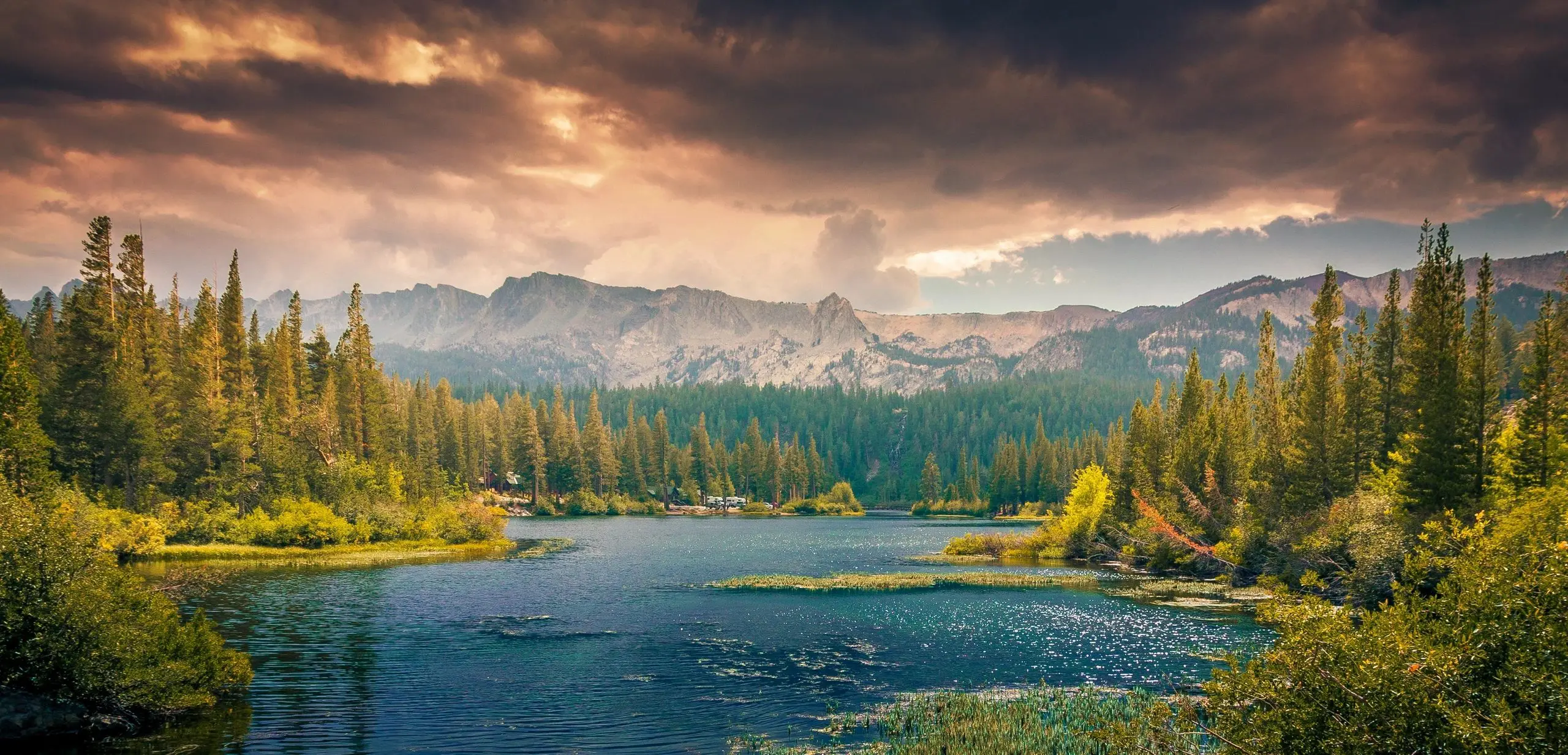 Sunset over a serene mountain lake surrounded by pine trees.